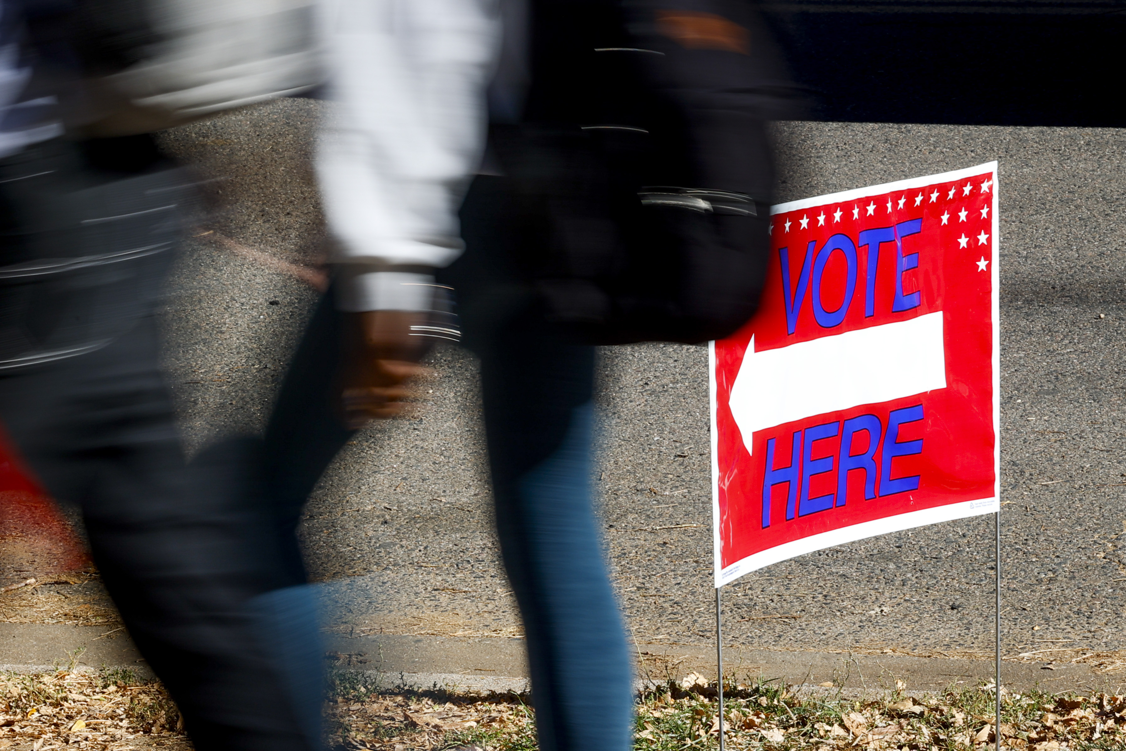 People walking past a vote here sign with an arrow