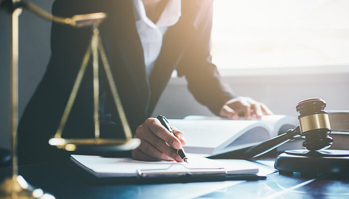 A suited woman writes on a notepad, near a gavel and scale