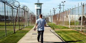 A man walks out of prison on a path between two barbed wire fences